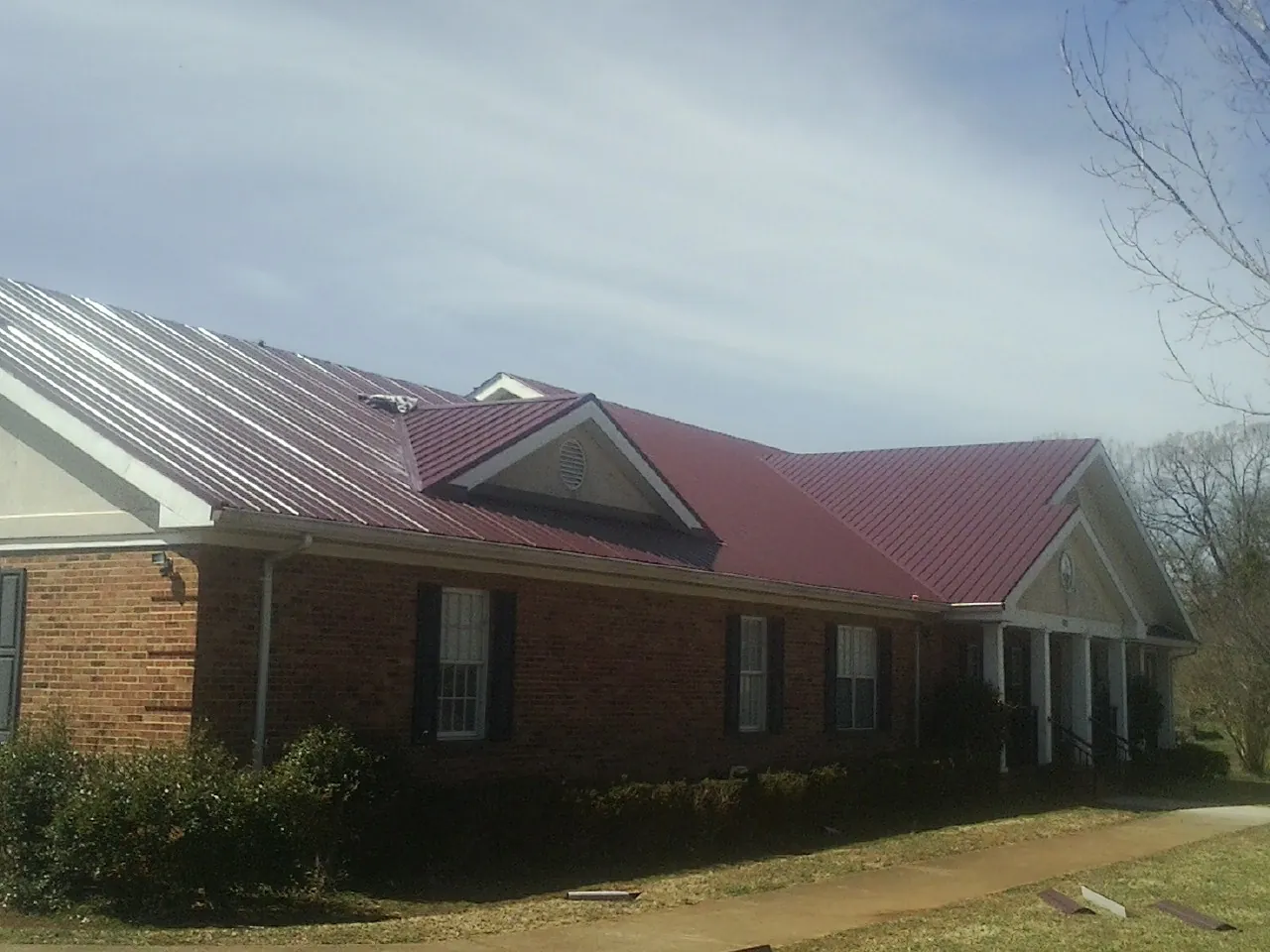 Red metal roof with gabled entries on a long brick building, from a Hail Damage Roof Repair job in Chino Valley