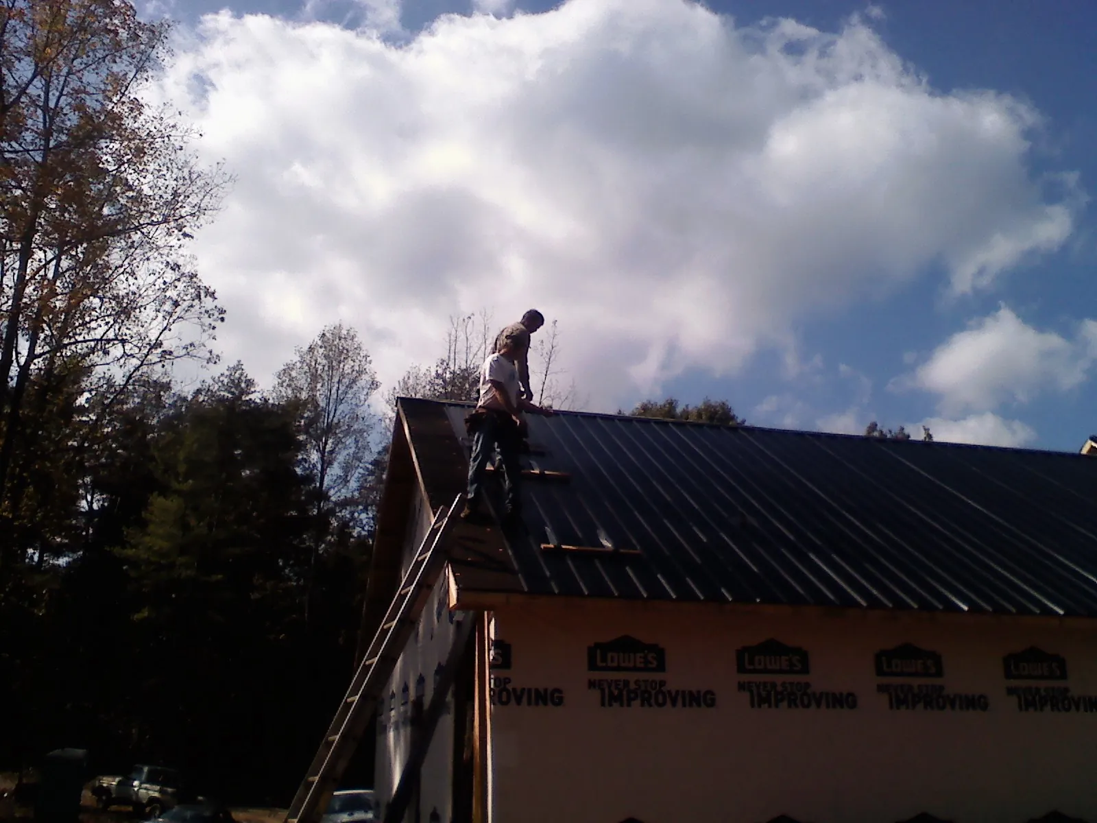 Roofer fastening dark metal panels high against a cloudy sky, from a Roof Inspection job in Chino Valley