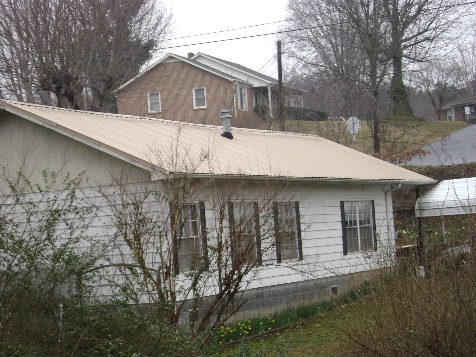Tan metal roof on a white sided house set into a hillside — Commercial Roofing by Roofing Brothers in Chino Valley